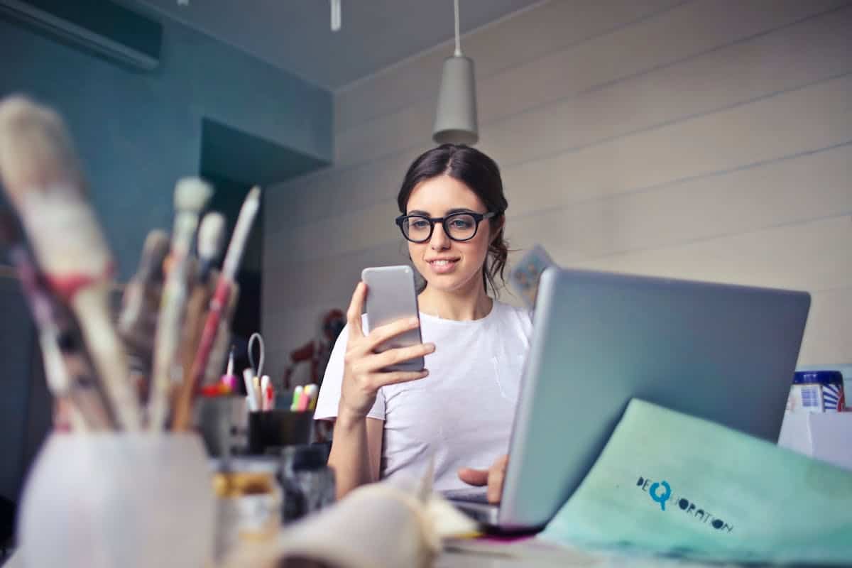 Mulher trabalhando em seu laptop e usando seu celular