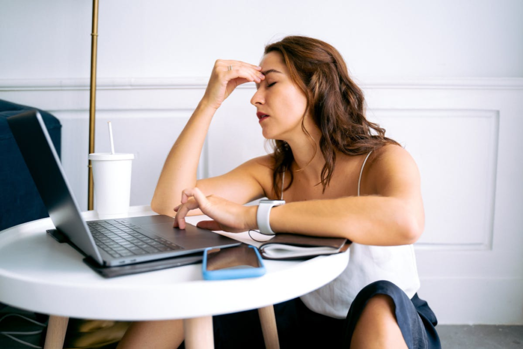 Mulher com mão na cabeça, de frente para o computador, parecendo cansada