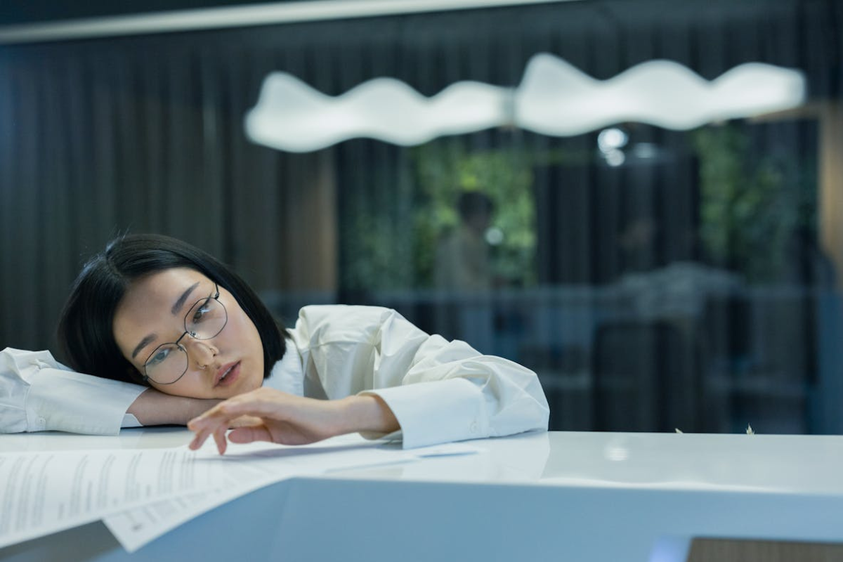 Mulher no trabalho, com corpo inclinado sobre sua mesa