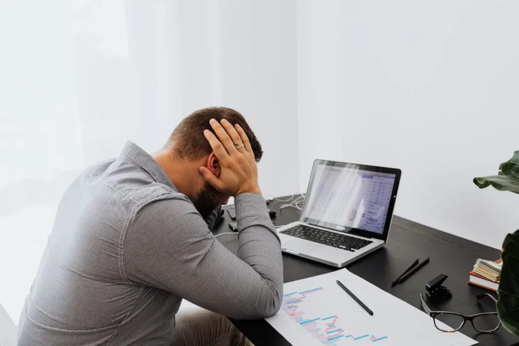 Homem de frente para o computador, com a mão na cabeça