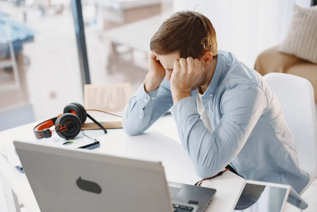 Homem de frente para o computador, com a mão na cabeça