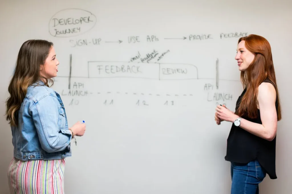 Duas mulheres conversando de frente para um quadro branco