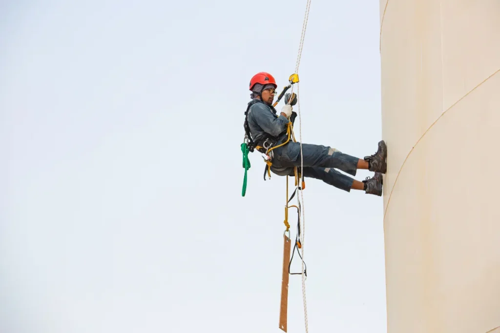 Trabalhador pendurado em prédio, usando equipamento de segurança.