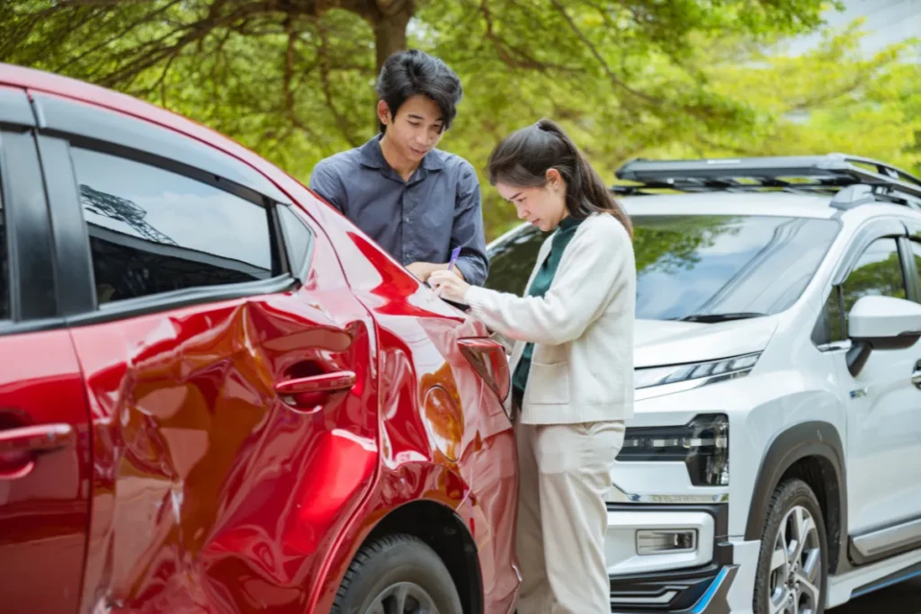 duas pessoas observando e anotando danos em um carro vermelho amassado após colisão