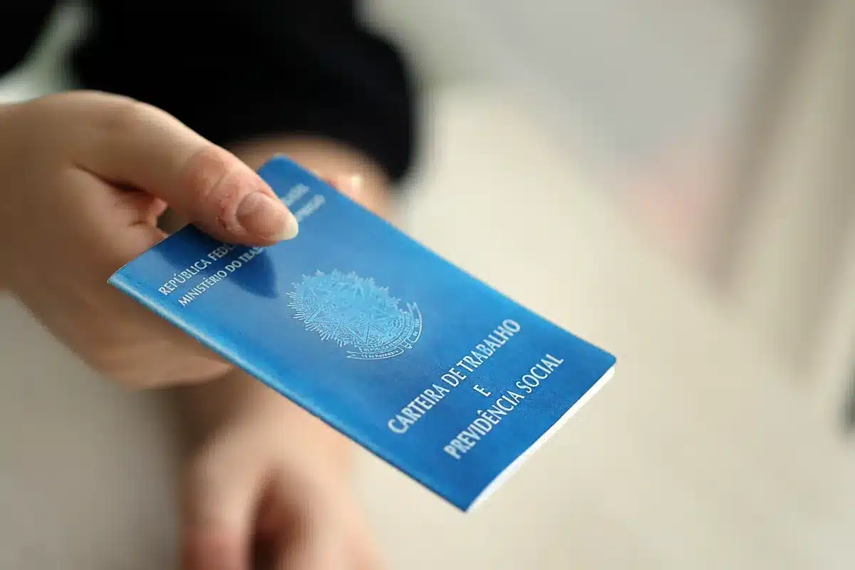 Pessoa segurando uma Carteira de Trabalho e Previdência Social azul nas mãos.
