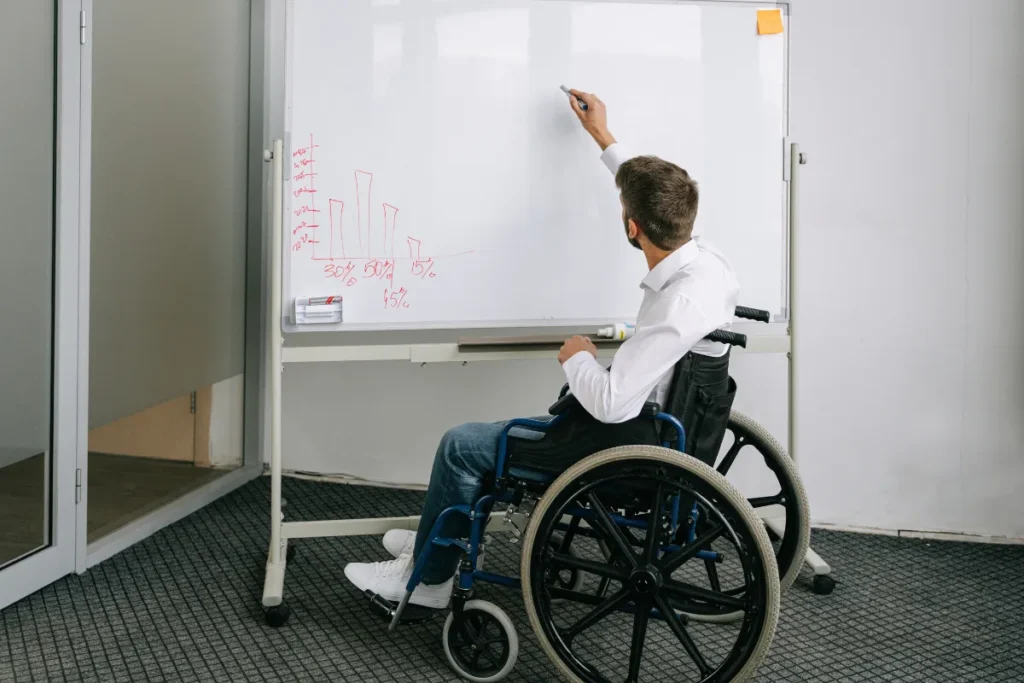 Homem em cadeira de rodas escrevendo em quadro branco durante apresentação em ambiente corporativo
