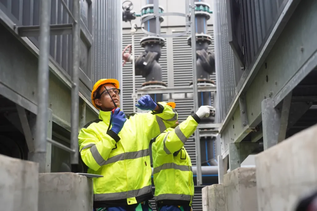 dois trabalhadores com equipamentos de proteção verificando estrutura e equipamentos industriais em área técnica