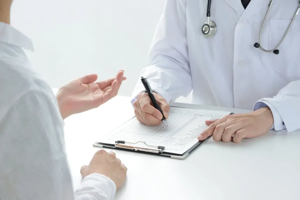 Médico de jaleco preenchendo formulário durante consulta com paciente em exame ocupacional.