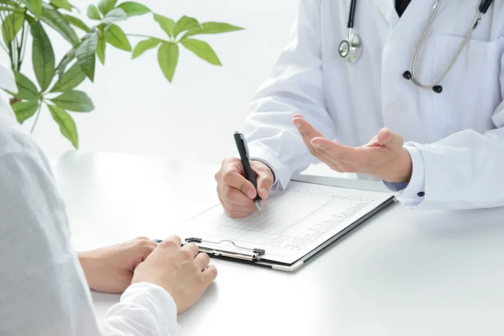 Médico com estetoscópio preenchendo formulário enquanto conversa com paciente durante consulta ocupacional.