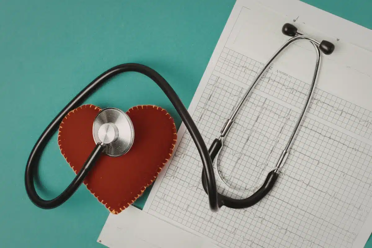 Estetoscópio sobre um gráfico médico ao lado de um objeto em formato de coração em fundo verde.