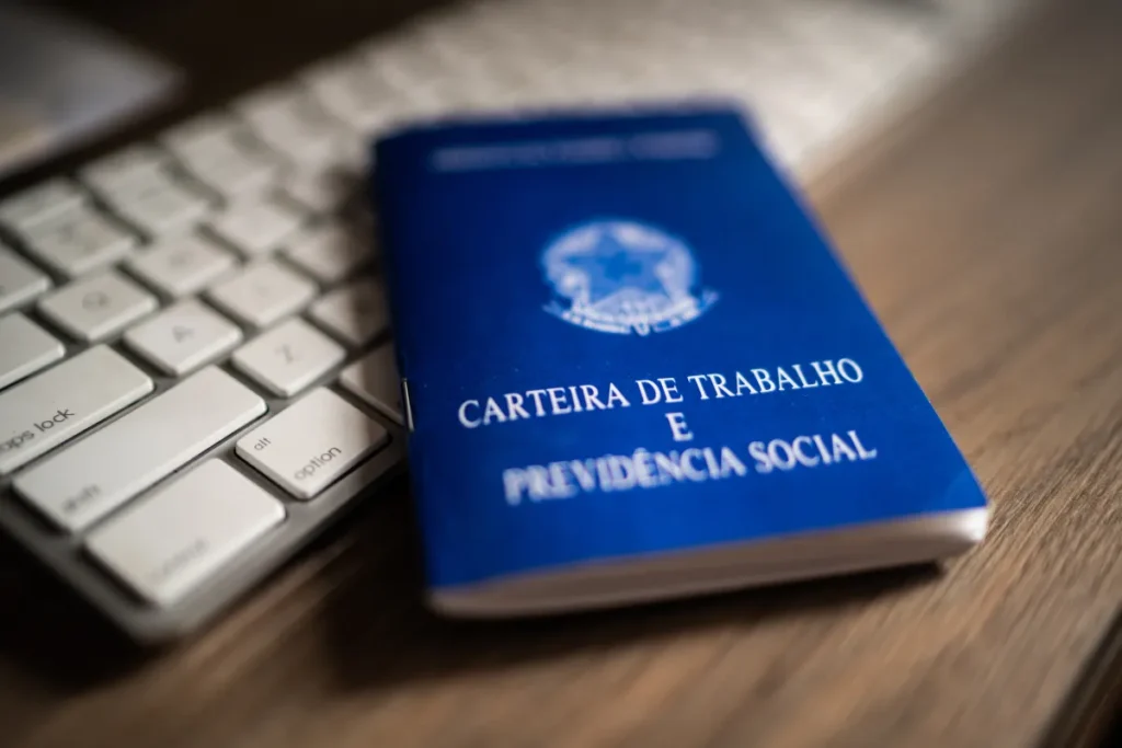 carteira de trabalho sobre mesa ao lado de teclado de computador
