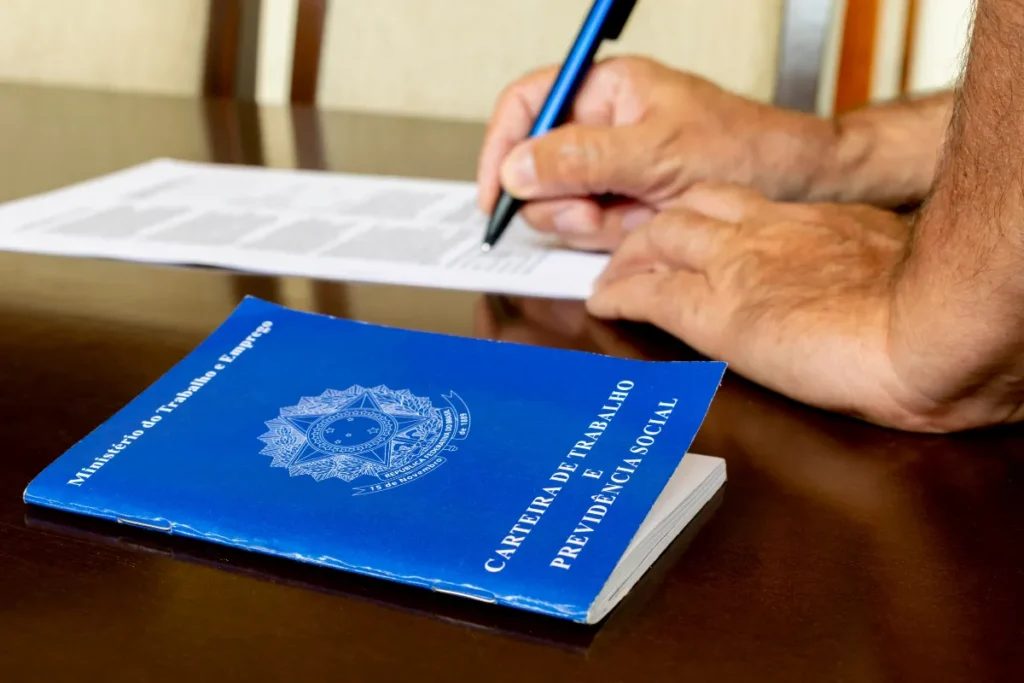 pessoa assinando documento com carteira de trabalho sobre a mesa