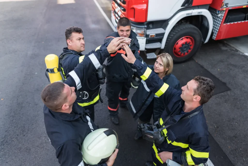 Equipe de brigadistas reunida ao lado de caminhão de bombeiros com mãos juntas em círculo