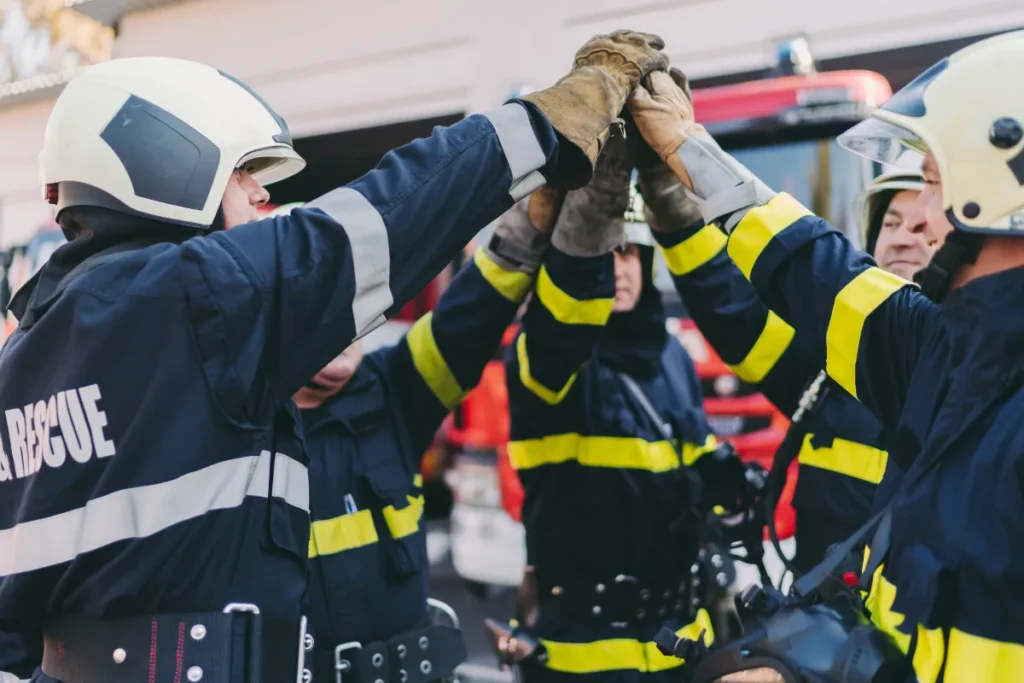Equipe de bombeiros com uniformes de proteção levantando as mãos juntas em sinal de união