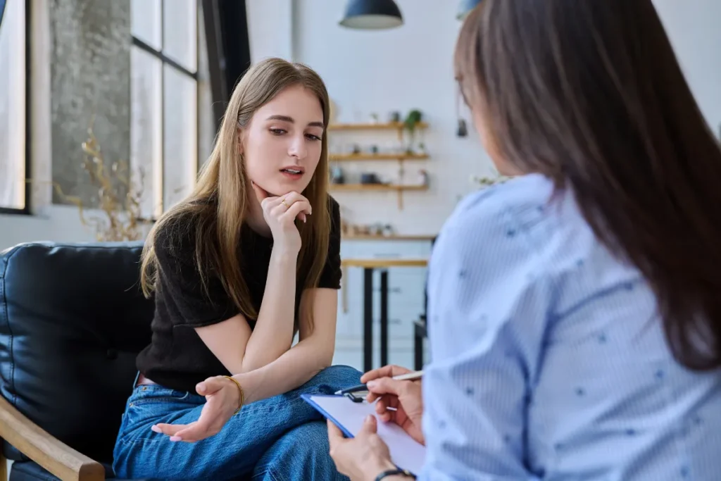 mulher jovem falando enquanto outra pessoa anota em prancheta durante conversa em ambiente tranquilo
