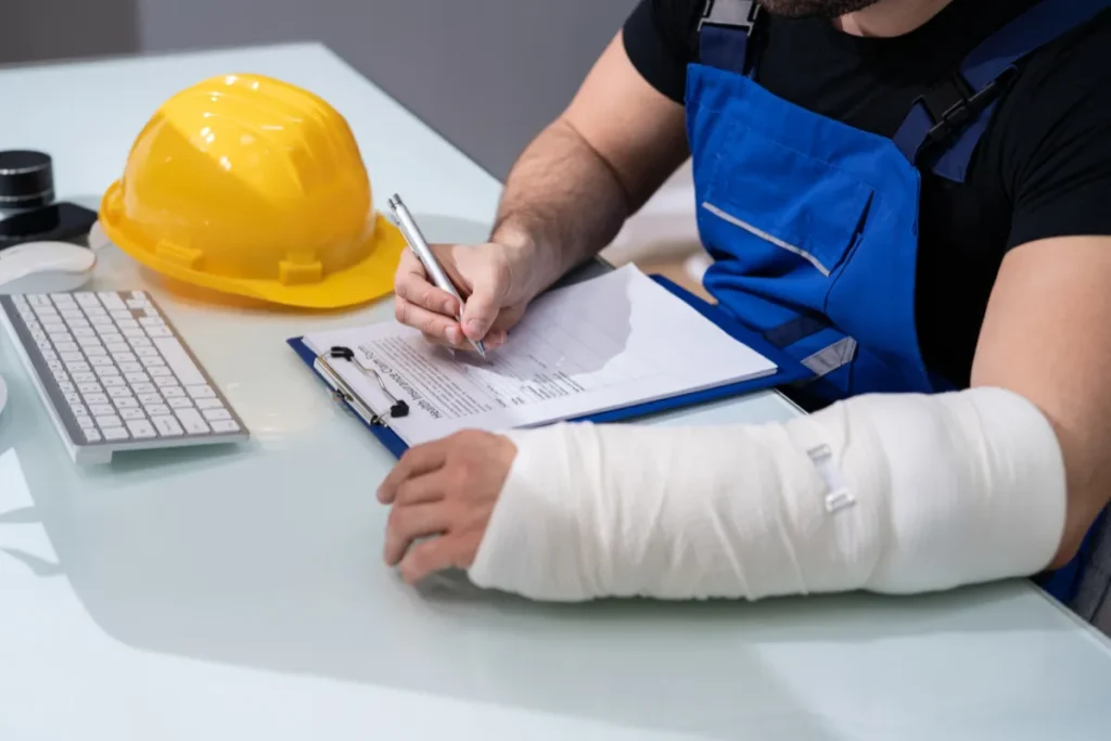 Trabalhador com braço imobilizado preenchendo documento ao lado de capacete de segurança