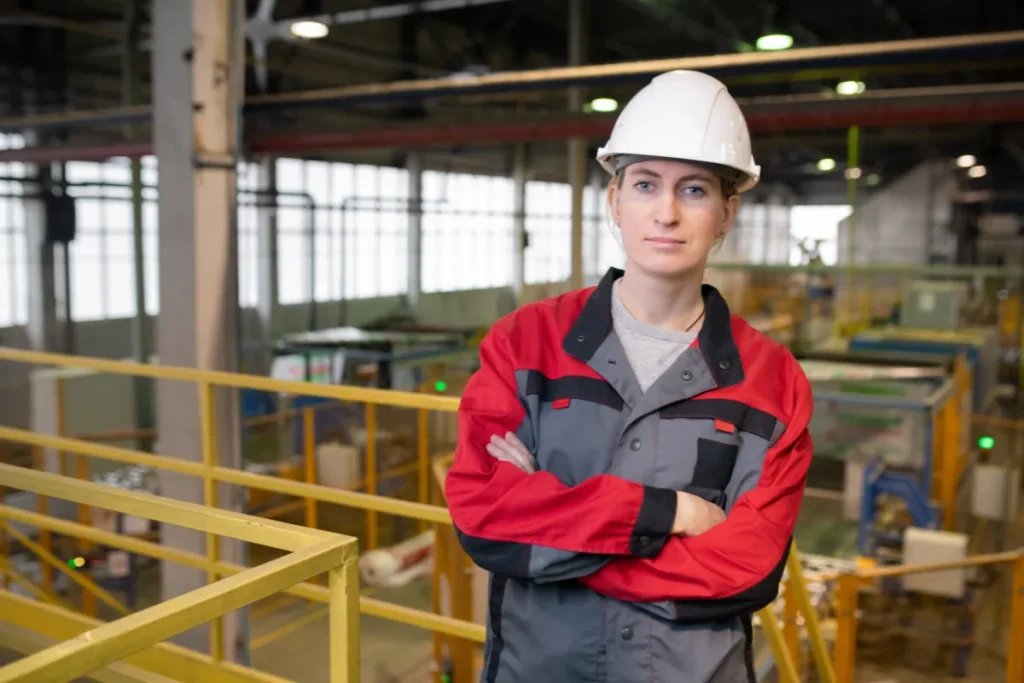 Profissional com capacete e uniforme de proteção em ambiente industrial com braços cruzados
