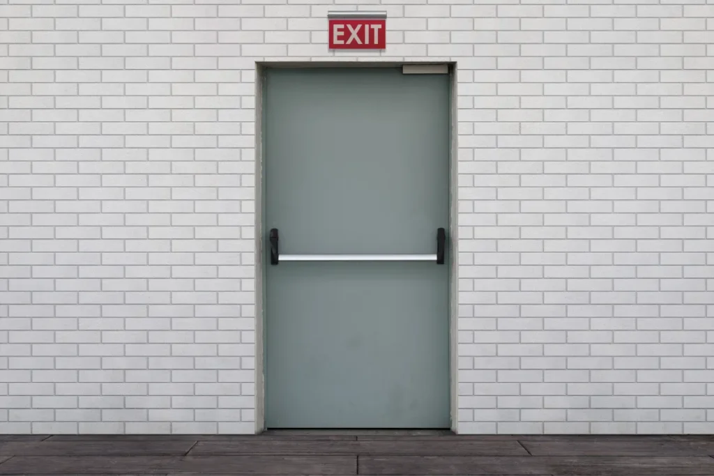 porta de saída de emergência com placa exit em parede branca e barra horizontal de abertura