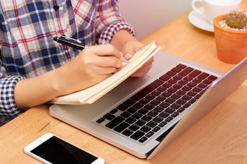Colaborador fazendo anotações ao lado do notebook durante atividade de SIPAT à distância em ambiente de home office.