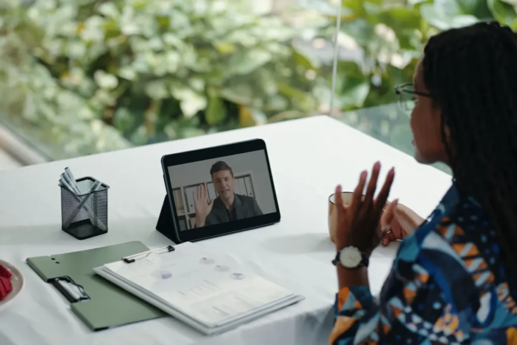 Profissional acompanha reunião de SIPAT online por videochamada com tablet e materiais de apoio sobre segurança do trabalho.