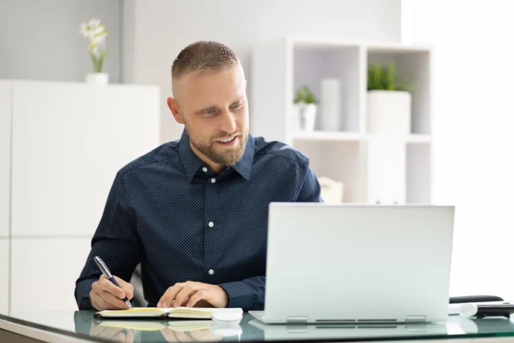 Profissional trabalhando em notebook e fazendo anotações durante o planejamento de uma SIPAT online corporativa.