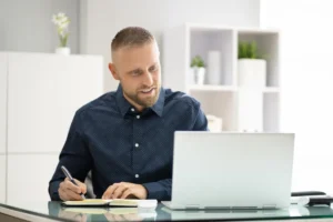 Profissional trabalhando em notebook e fazendo anotações durante o planejamento de uma SIPAT online corporativa.