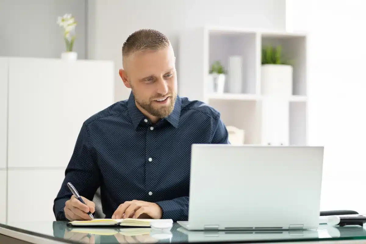Profissional trabalhando em notebook e fazendo anotações durante o planejamento de uma SIPAT online corporativa.