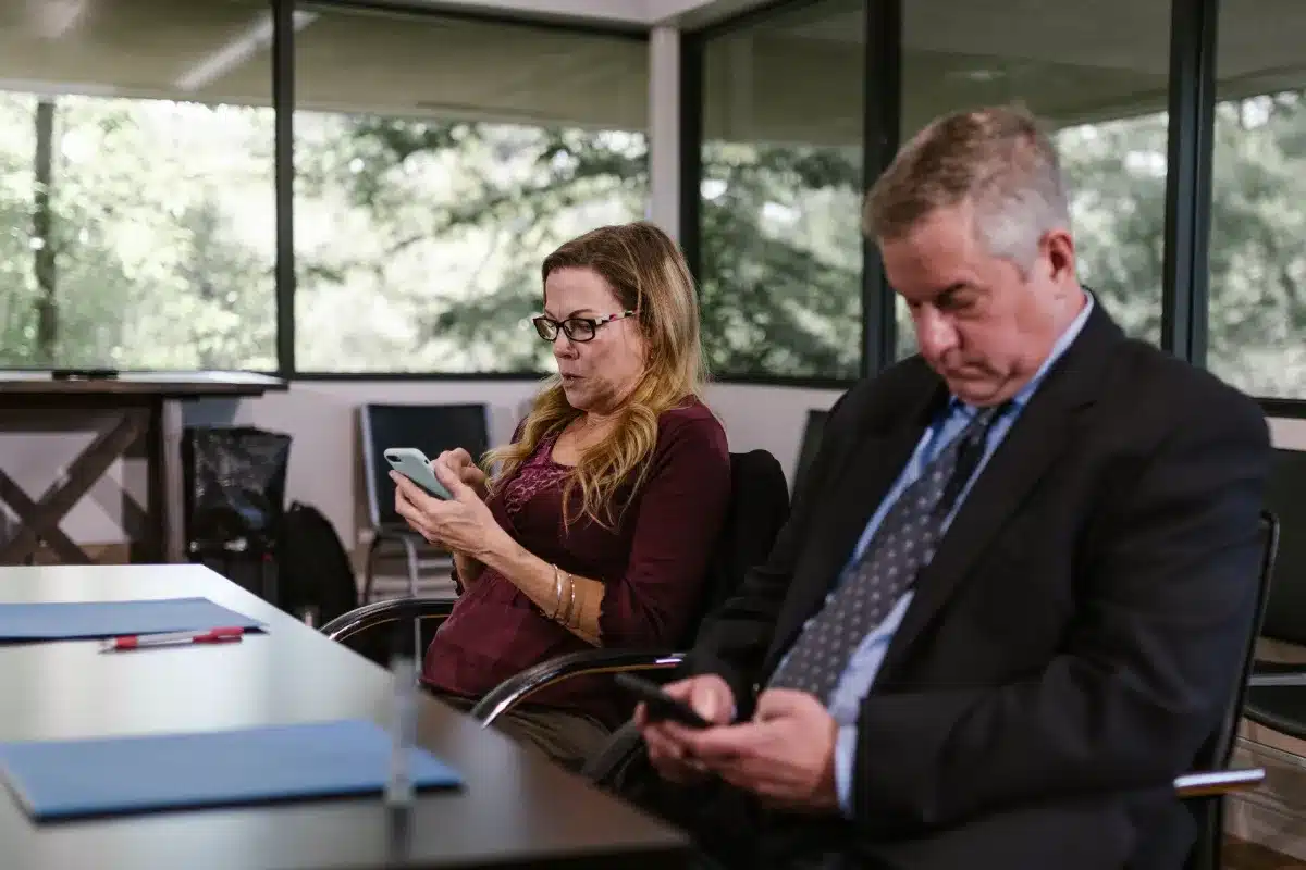 Dois profissionais sentados em reunião usando smartphones