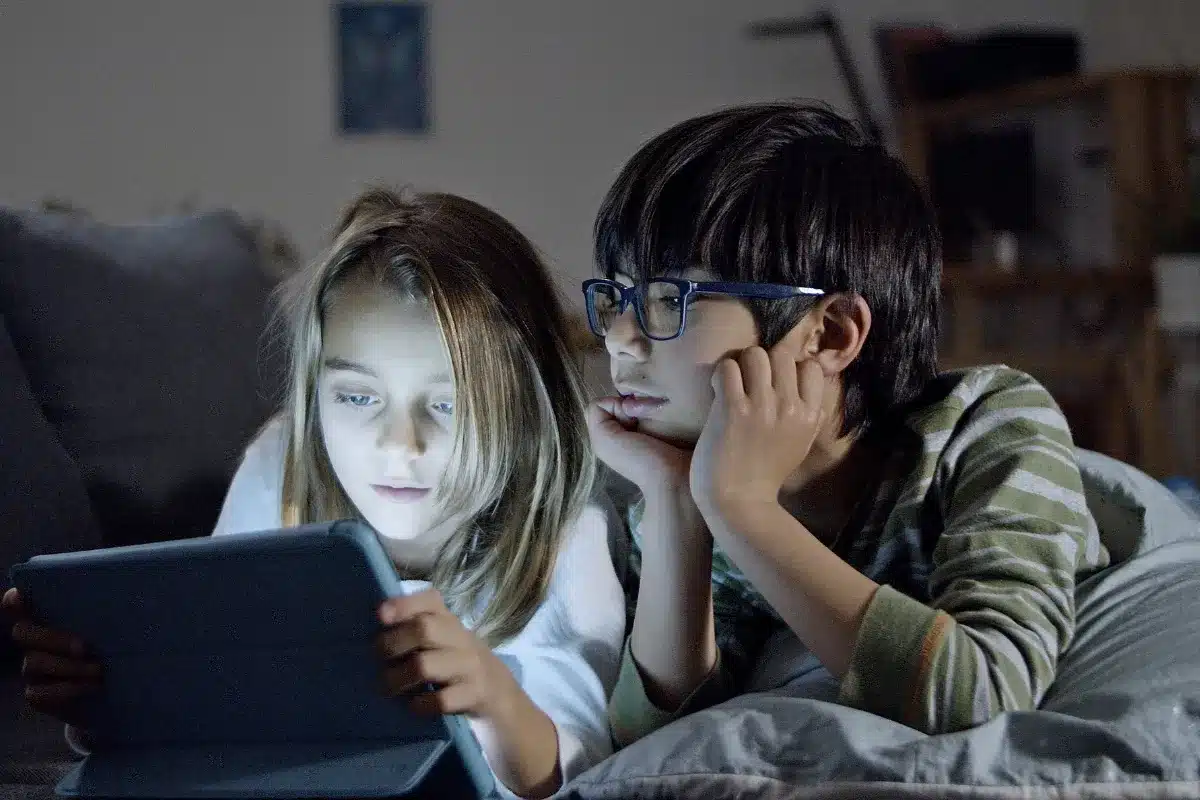 Duas crianças usando um tablet em um quarto durante a noite