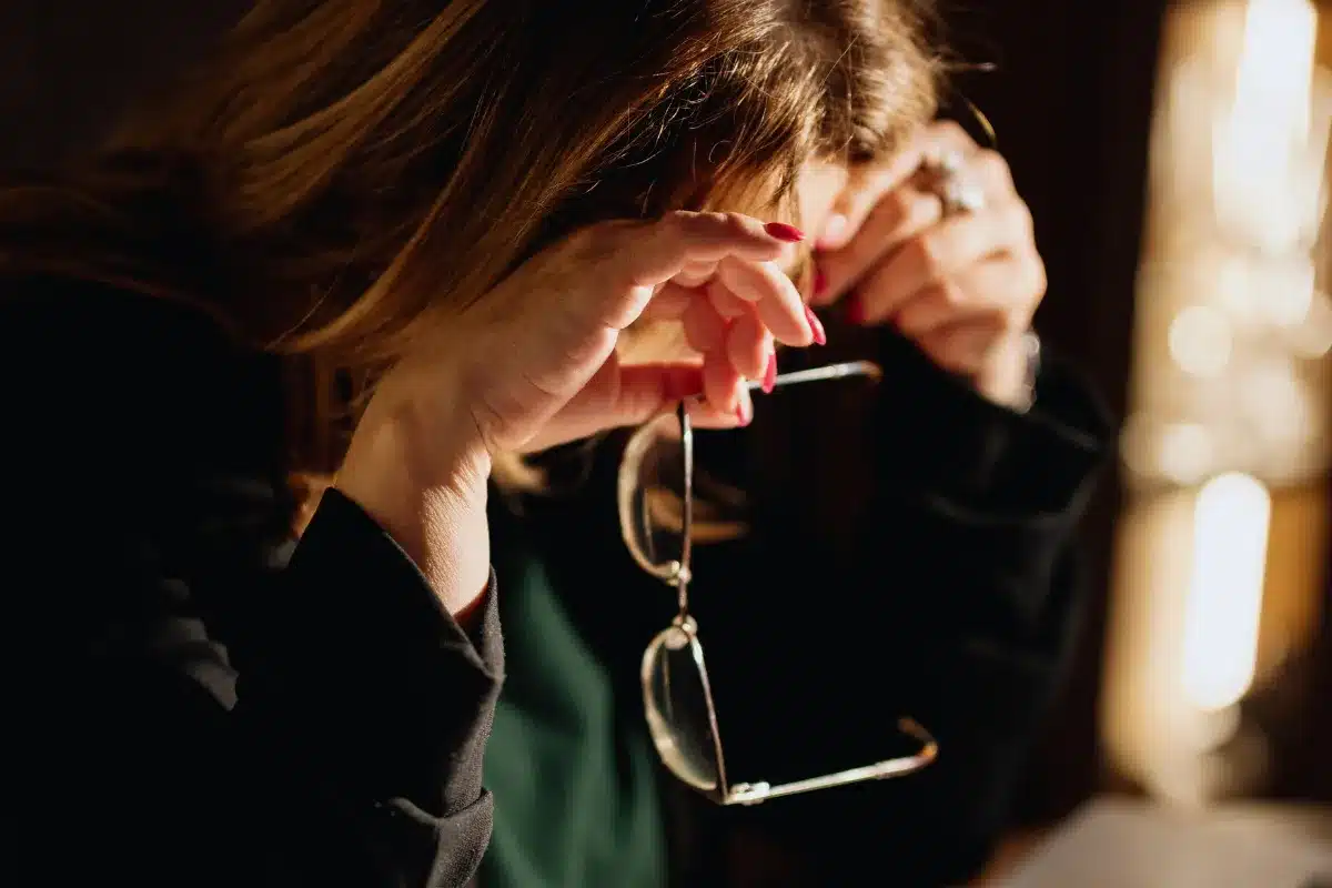 Mulher com expressão de cansaço segurando os óculos durante uma pausa