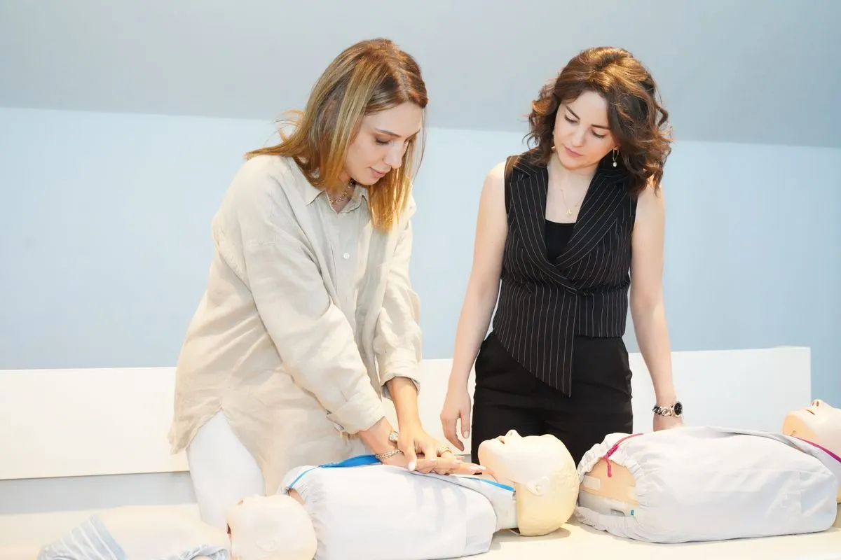 Duas mulheres praticam reanimação em bonecos de treinamento numa sala de curso