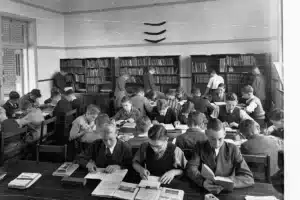Estudantes acompanhando aula em uma sala de formação técnica, com cadernos e equipamentos de estudo.