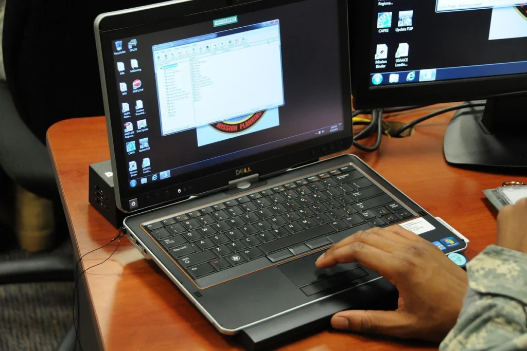 Mãos digitam em um notebook sobre uma mesa de estudo.