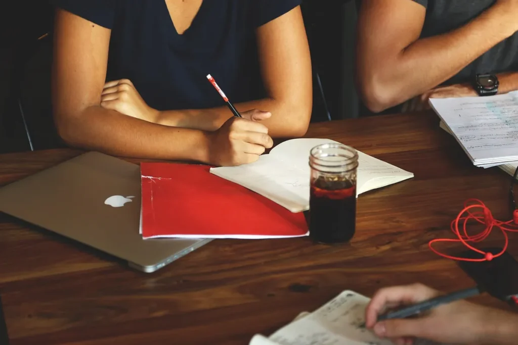 Colegas em volta de uma mesa de trabalho com notebook, pastas e anotações.