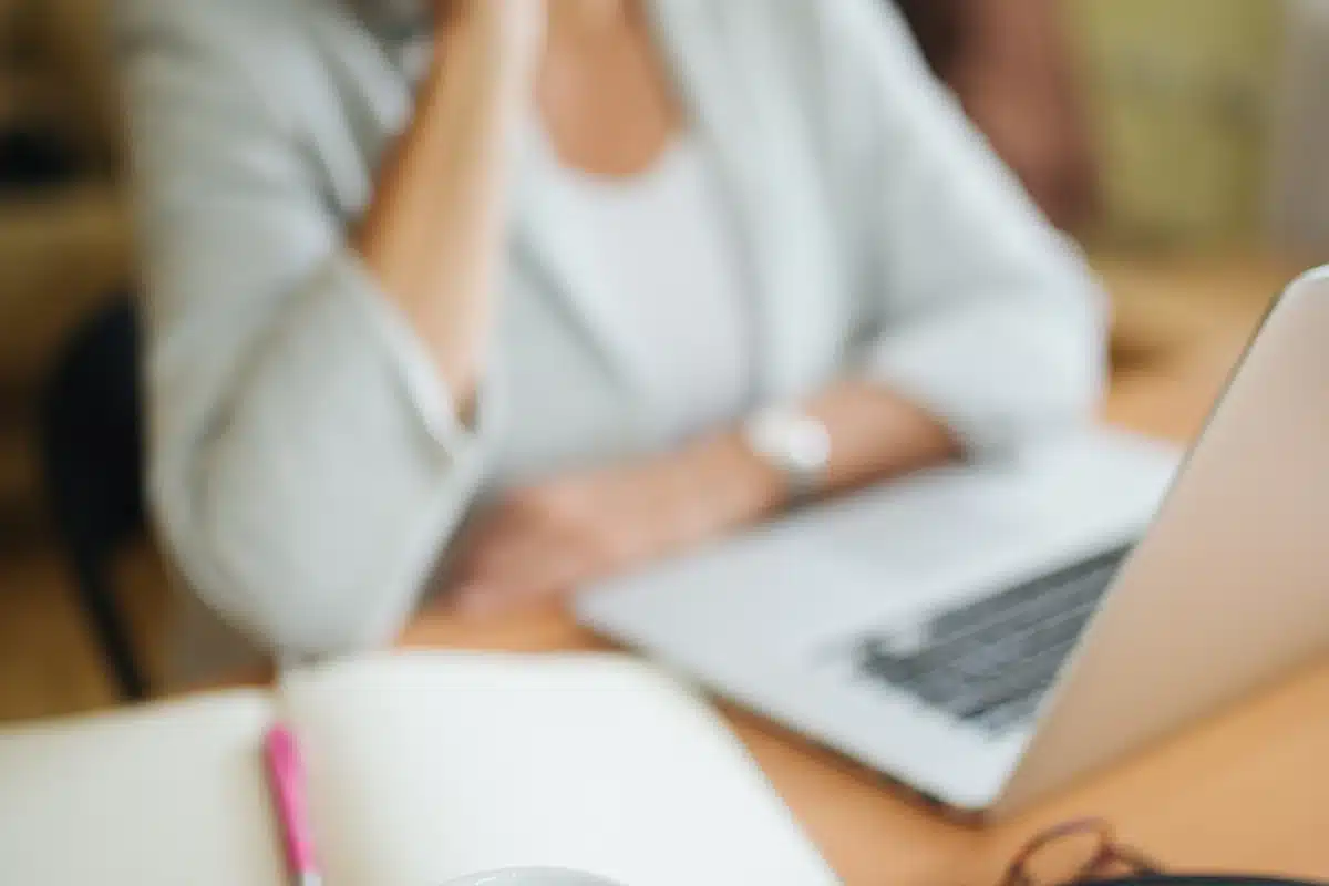 Xícara de café sobre a mesa do escritório e, ao fundo, uma mulher ri ao telefone