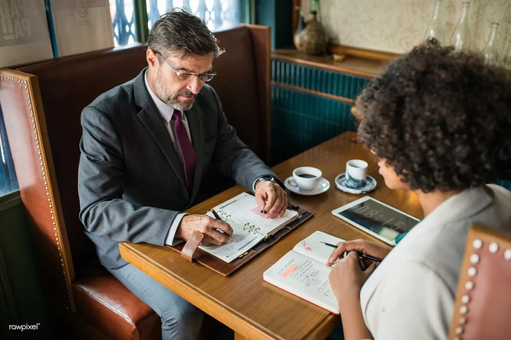 Dois colegas conversam e fazem anotações numa mesa de café