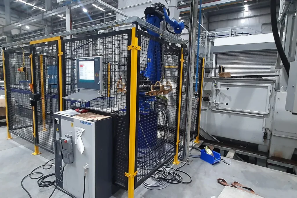 Célula de máquina automática cercada por grade de proteção amarela dentro de um galpão industrial