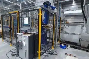 Célula de máquina automática cercada por grade de proteção amarela dentro de um galpão industrial
