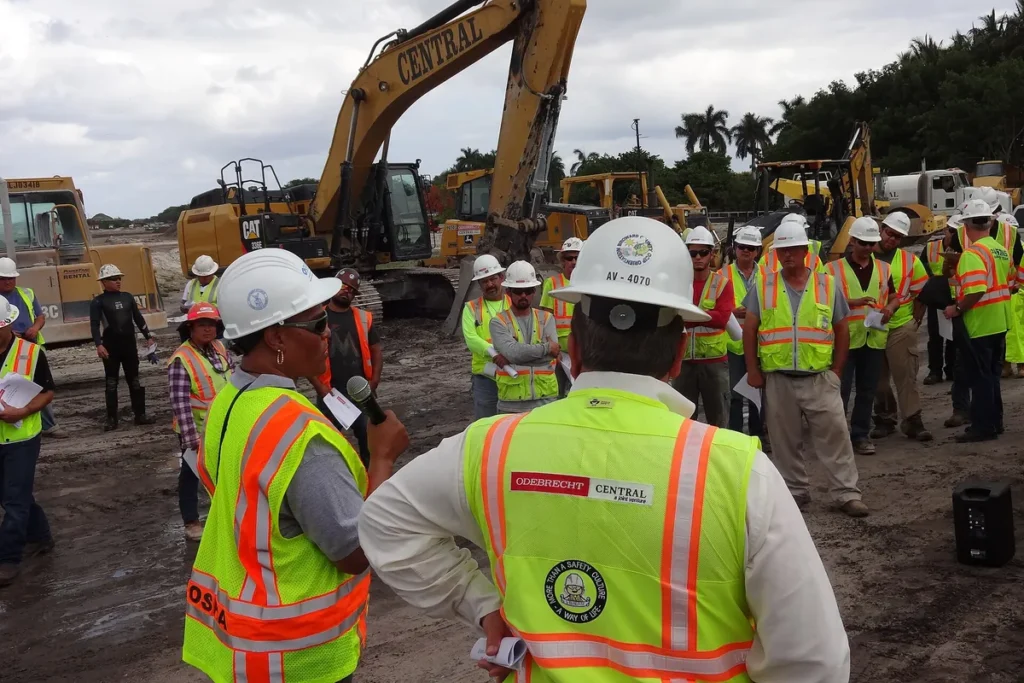 Trabalhadores com capacete e colete refletivo reunidos em orientação de segurança num canteiro de obras