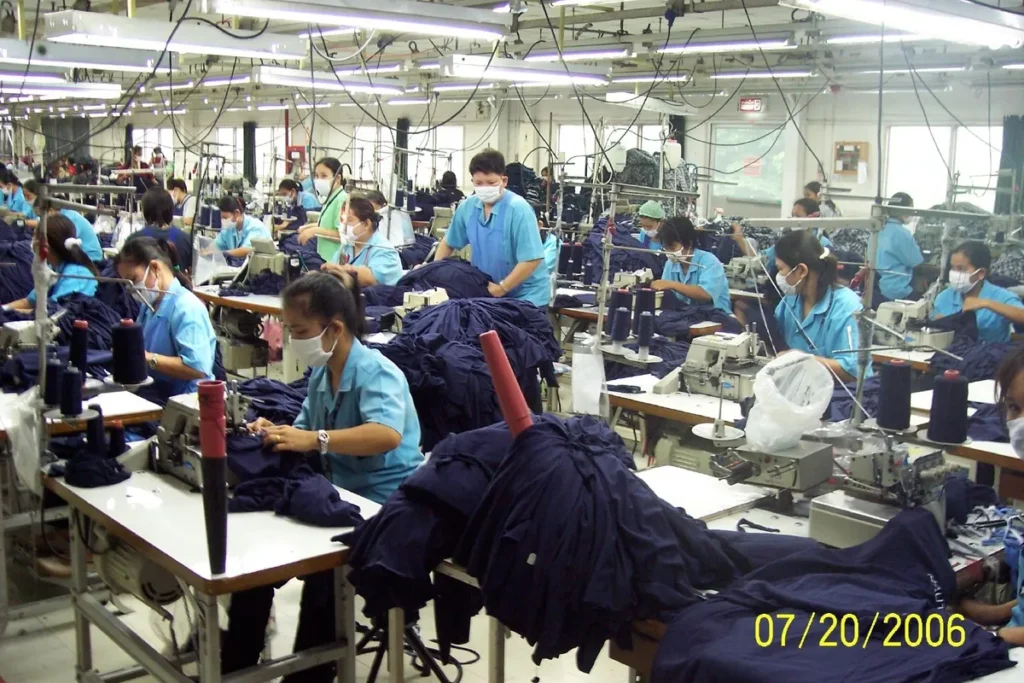 Linha de costura industrial com dezenas de trabalhadoras operando máquinas ao mesmo tempo