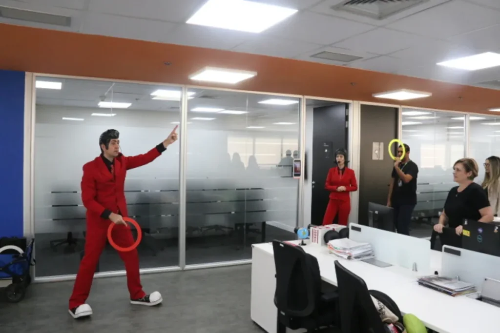 Facilitador caracterizado em terno vermelho conduz dinâmica do 5W2H com colaboradores em escritório