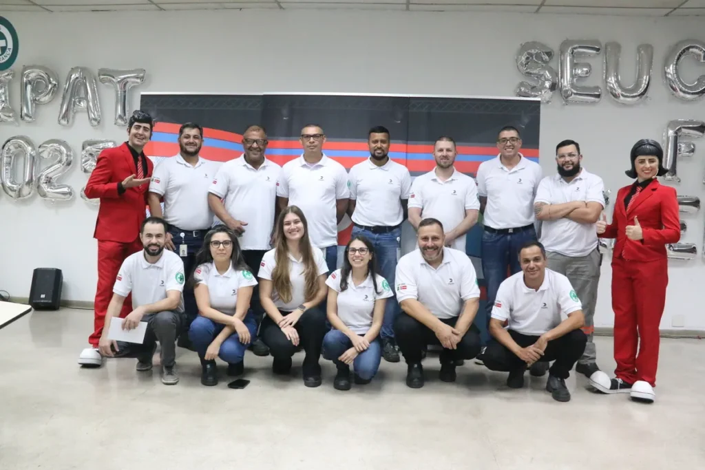 Grupo de 15 profissionais em evento de segurança do trabalho com balões de CAT, Sipat e Seu Futuro.