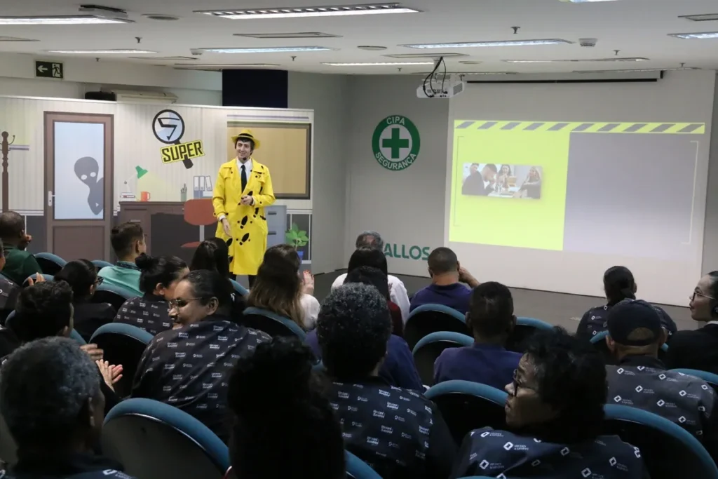 Palestrante com figurino amarelo realizando treinamento de segurança do trabalho para funcionários em auditório