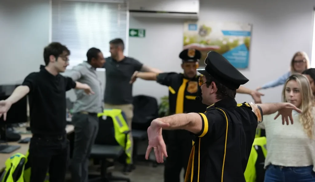Instrutor vestido com uniforme preto e amarelo conduzindo grupo de colaboradores em uma atividade de alongamento e integração no ambiente de trabalho.