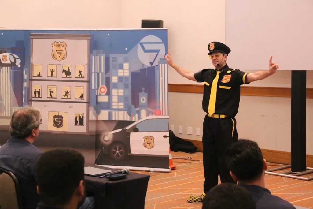 Palestrante de uniforme em frente a uma plateia. Foto de uma reunião de treinamento ou evento corporativo com público sentado em mesas em uma sala de conferências.