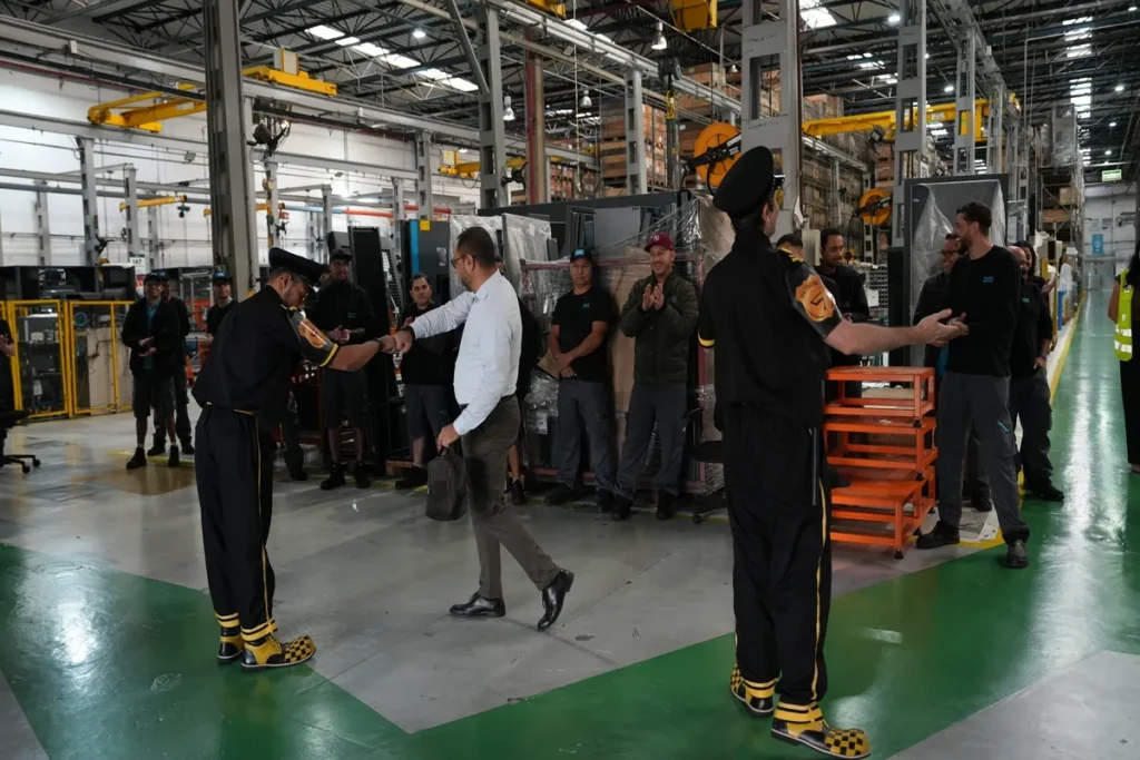 Instrutor de segurança de uniforme apertando a mão de trabalhador em palestra ou treinamento de NR 01, em ambiente de fábrica ou armazém industrial.