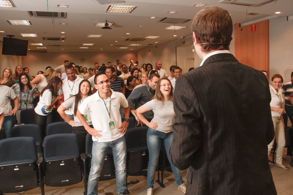 Palestrante em ambiente análogo à sala de reuniões fazendo dinâmica com público que sorri durante Palestra sobre assédio sexual