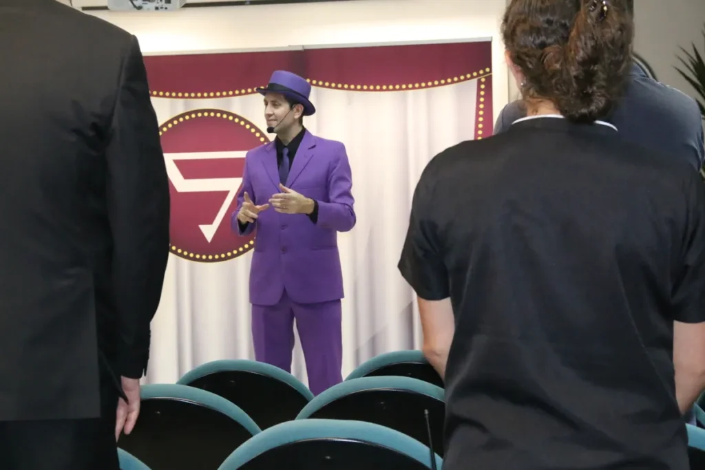 Apresentador usando terno roxo e chapéu conduz palestra interativa durante evento SIPAT em auditório corporativo