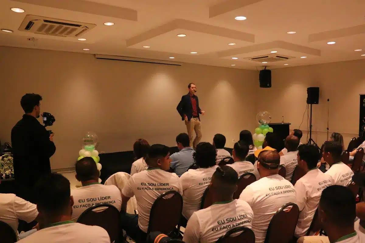 Palestrante masculino caminhando no palco durante um evento de liderança, dirigindo-se a uma plateia que veste camisetas com a frase "Eu sou líder, eu faço a diferença," ilustrando a importância da liderança na resposta a emergências como a anafilaxia.