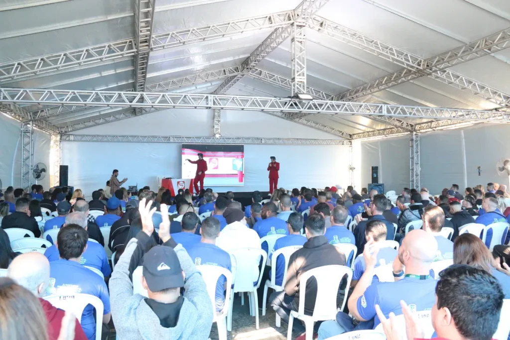 Grande público assiste a palestra sobre apneia do sono em auditório coberto, com palestrantes vestidos de vermelho no palco.